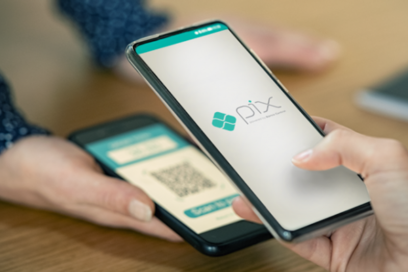 mãos seguram dois celulares com QR Code para pagamento via pix