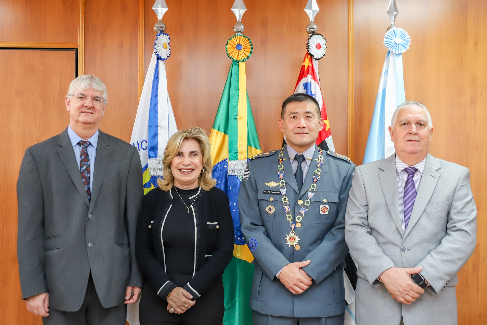 Homenageado possa para foto ao lado dos desembargadores Edison Pelegrini, Ana Paula e Helcio Dantas em frente a uma parede de madeira e quatro bandeiras