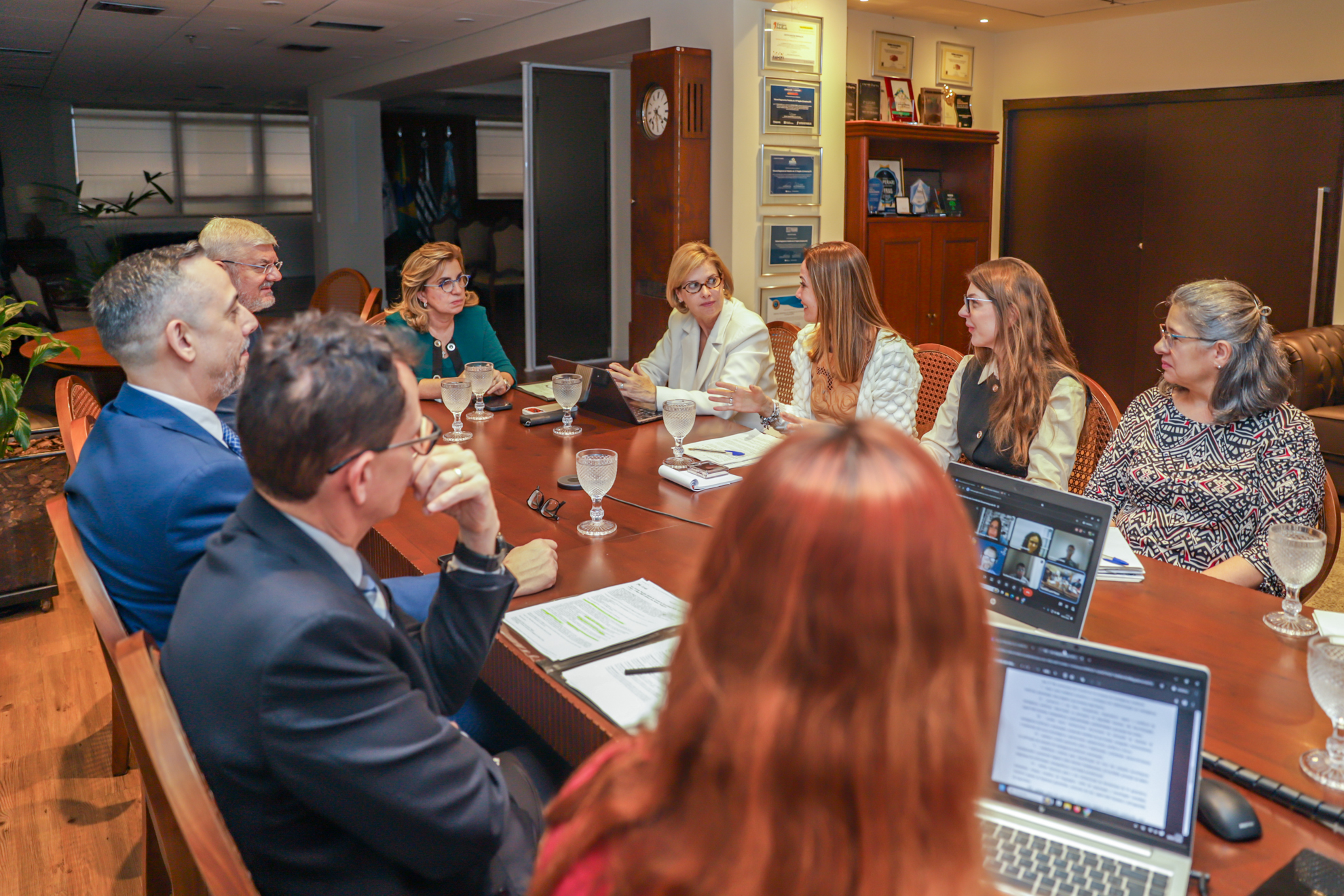 Pessoas sentada em volta de uma mesa oval participam de uma reunião.